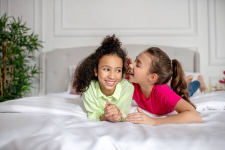 Secrets. Two girls laying on the bed sharing secrets