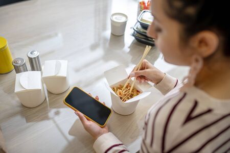 Indoors. Woman hands holding phone and chopsticks in the kitchen