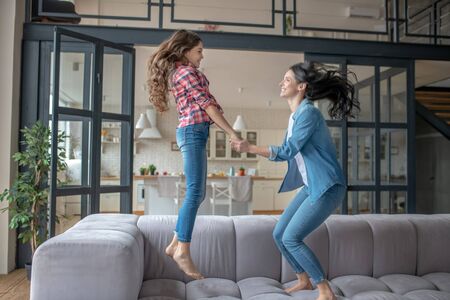 Jumping. Mom and daughter holding hands and jumping on the sofa