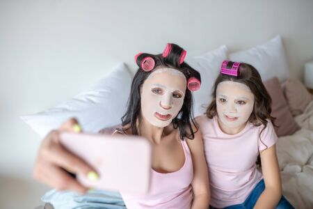 Making a picture. Mom and daughter with facial mask on their faces making a pictureの写真素材