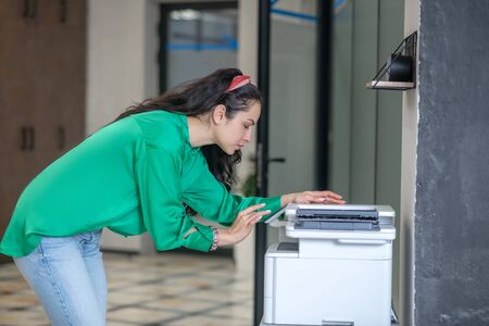 Copy machine. Young woman in jeans and a green blouse bending over a copy machine, serious...