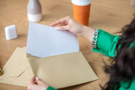Papers and envelope. Female beautiful hands with manicure holding a letter and an envelope over the table.の写真素材