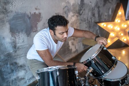 Drummer. Dark-haired young man in a white tshirt standing near the drums