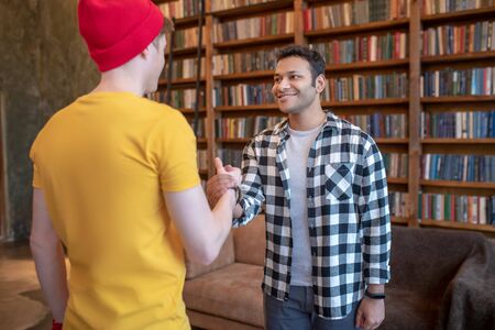 Two friends. Two young handsome men looking contented shaking handsの写真素材