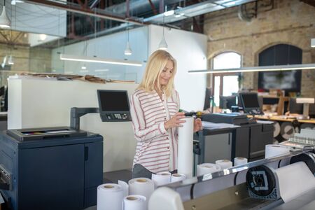 At workshop. Blonde woman standing in paper printing workshop, holding roll of paper