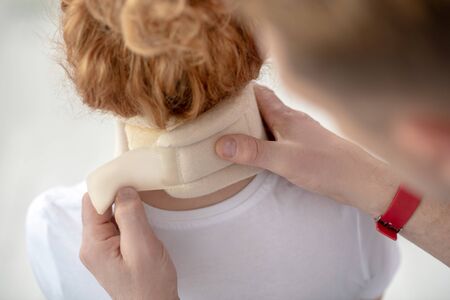 At rehabilitation center. Male physiotherapist hands fixing neck bandage on female patient