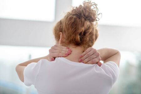 At rehabilitation center. Red-haired female patient massaging her painful neck