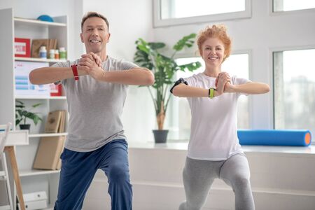 At rehabilitation center. Female patient and male physiotherapist lunging synchronically, smiling