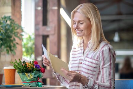 At work. Happy blonde woman received letter and flowers, smiling