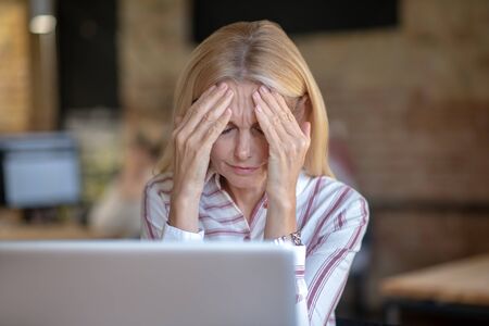 Modern office. Blonde woman suffering from headache, holding her forehead