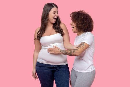 Woman in a top with bare shoulders touching her girlfriend arm, who is athletic in body with a...
