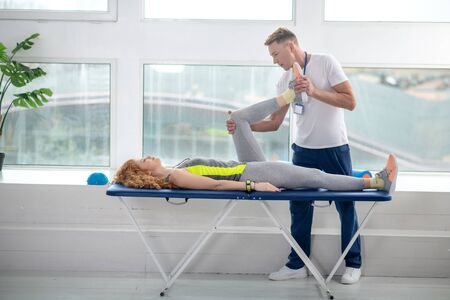 At rehabilitation center. Male physiotherapist treating leg of female patient