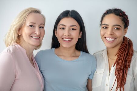 Three women. Three women standing near the wall smiling nicely