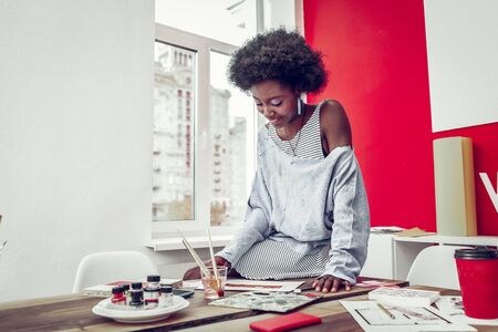 Feeling happiness. Cute African American girl keeping smile on her face and looking downwardsの写真素材