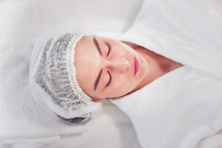 Waiting for cosmetologist. Top view of woman wearing white bathrobe closing eyes and waiting for cosmetologistの写真素材