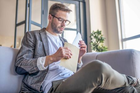 Opening the envelope. Stylish fair-haired man opening the envelopeの写真素材