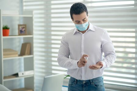 Disinfection. Man in a white shirt disinfecting his tablet and looking involvedの写真素材