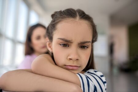 Conflict. Face of a sad upset little girl with brown eyes, turned away from her mother, at home.
