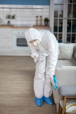 Furniture disinfecting. Woman in white workwear and protective eyeglasses disinfecting furnitureの写真素材