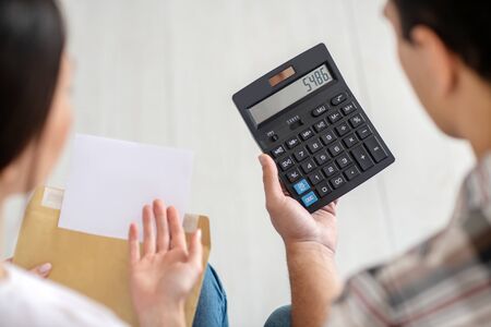 Calculation process. Close-up of male and female hands holding calculator and envelope