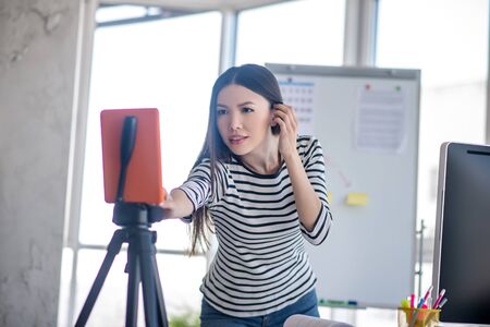 Recording. Dark-haired girl in a striped shirt fixing the camera