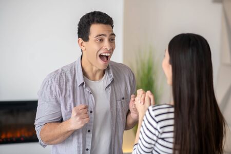 Young happy man laughing with open mouth standing in front of a dark-haired wife, they are at home.の写真素材
