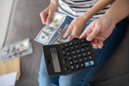 Cash counting. Male strong hand holding out a calculator, female hands holding and counting banknotes.の写真素材