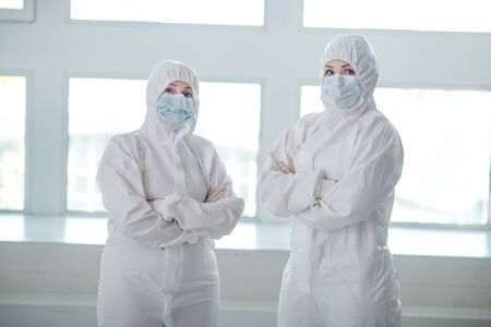 Protective measures. Medical workers in protective clothing and medical masks standing with their arms foldedの写真素材