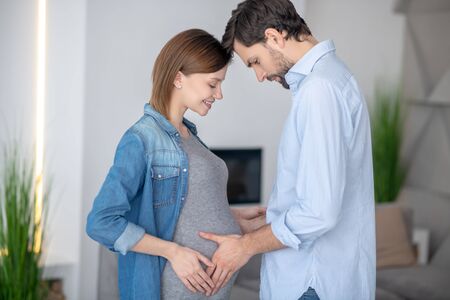 happiness. Young dark-haired man touching his wifes pregnant abdomen