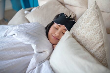 At home. Young brunette sleeping peacefully in bed, wearing sleep mask