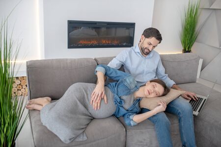 Relaxing. Young pregnant woman in a jeans jacket feeling sleepy laying on her husbands lapsの写真素材