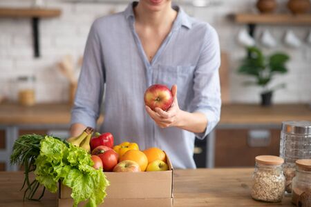 In the kitchen. Woman in grey homewear standing in the kitchen with apple in her handの写真素材