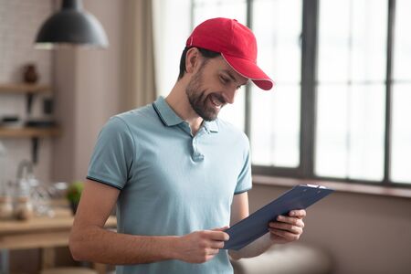 Good day. Delivery person in a red hat looking at the waybill and smilingの写真素材