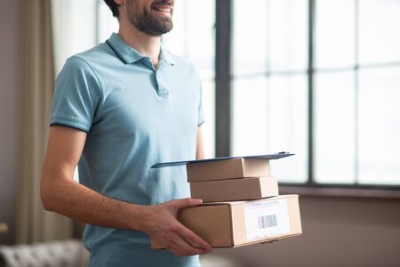 Boxes in hands. Delivery person standing in the kitchen and holding the boxes in his handsの写真素材
