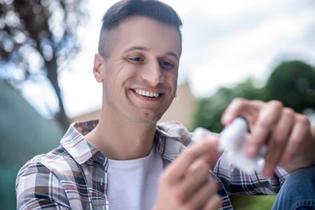 Free time. Smiling dark-haired male taking wireless earphones from the boxの写真素材