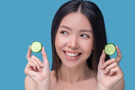 Natural cosmetics. Smiling cute young woman holdingslices of cucumberの写真素材