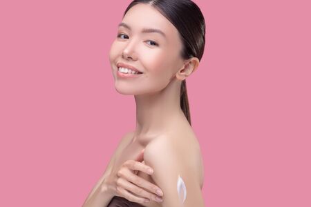 Body care. Pretty asian girl applying cream on her body and smilingの写真素材