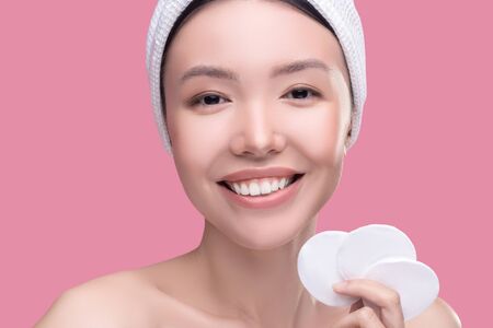 Face cleaning. Smiling asian girl in a white headscarf holding sponges for cleaningの写真素材