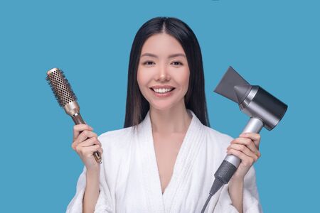 Hair care. Brunette young asian woman holding a brush and a hair dryerの写真素材