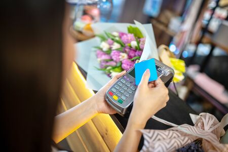 Flower shop. Close-up of female hands holding holding credit card and payment terminal