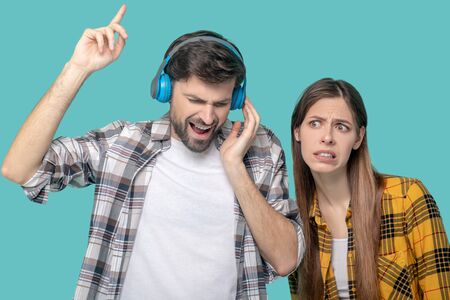 Inspired singing bearded man in headphones holding his hand up high and a displeased girl with a sad grimaceの写真素材