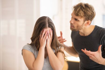 Scandal. Young long-haired woman closing her face while her husband shouting