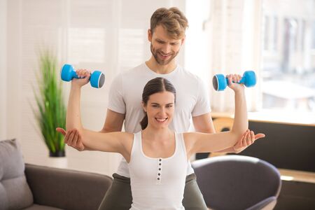 Home workout. Smiling woman working on her muscles and her husband helping herの写真素材