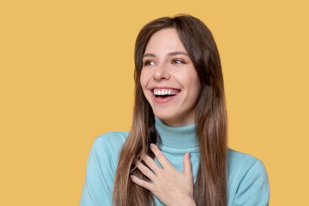 Fun mood. Cheerful young adult girl smiling, looking away touching her hand to yourself