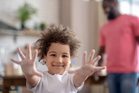 Excited. Pretty curly-haired kid showing her hands stained with flour and looking happyの写真素材