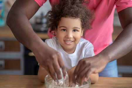 Enjoying. Cute kid with curly hair looking happy putting her hands into the bowl with flowerの写真素材