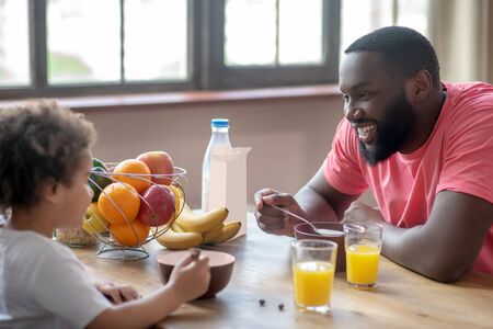 Feeling good. Dark-haired african american father having breakfast with his daughter and smilingの写真素材