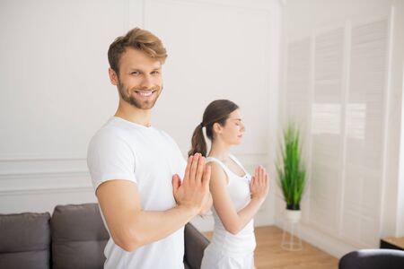 Yoga. Young couple in white tshirts putting their hands in namaste, young man smilingの写真素材