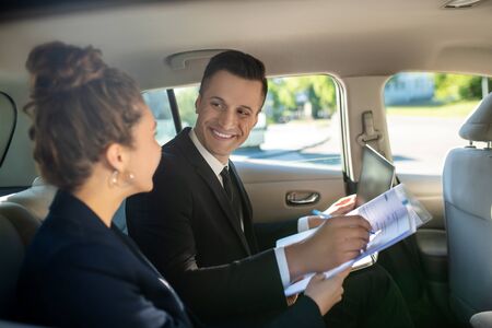 Doing business. Attractive smiling man in a suit signing document and woman from the back, sitting...