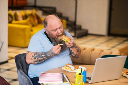 Eating. Bald fat man opening his mouth to bite a piece of burgerの写真素材